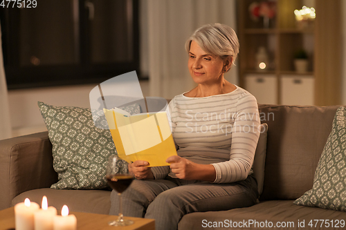 Image of happy senior woman reading book at home in evening