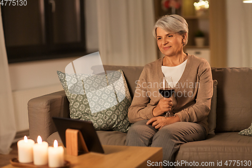 Image of senior woman with tablet pc drinking wine at home