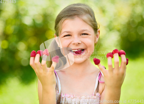 Image of Young girl is holding raspberries on her fingers