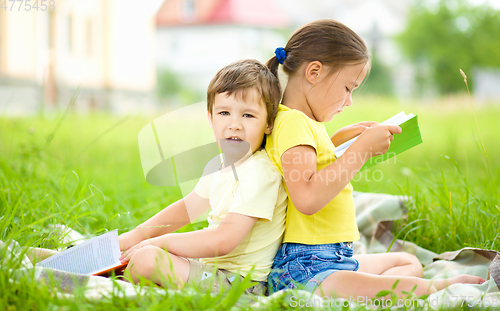 Image of Little girl and boy are reading book outdoors