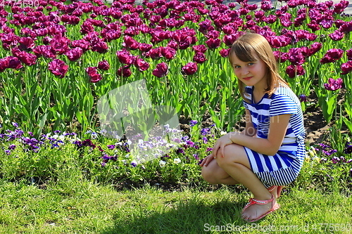 Image of little girl sitd by lilac tulips