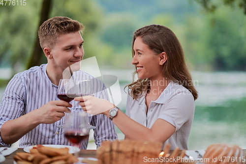 Image of couple toasting red wine glass while having picnic french dinner party outdoor