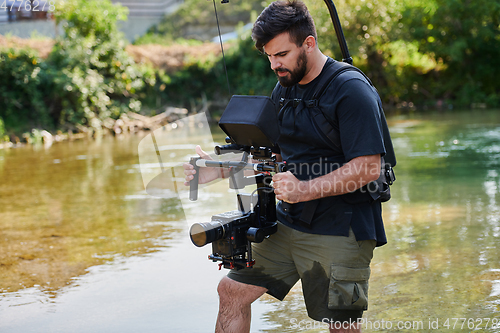 Image of a professionally equipped cameraman shoots in the water surrounded by beautiful nature.