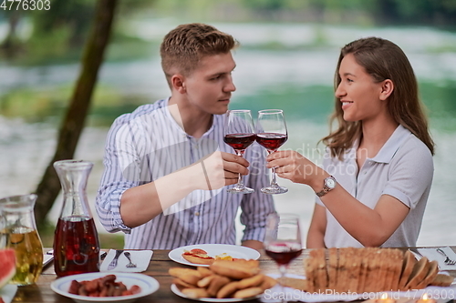Image of couple toasting red wine glass while having picnic french dinner party outdoor