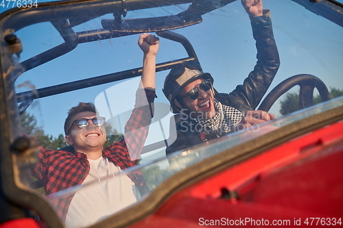 Image of two young happy excited men enjoying beautiful sunny day while driving a off road buggy car