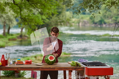 Image of man cutting juicy watermelon during outdoor french dinner party