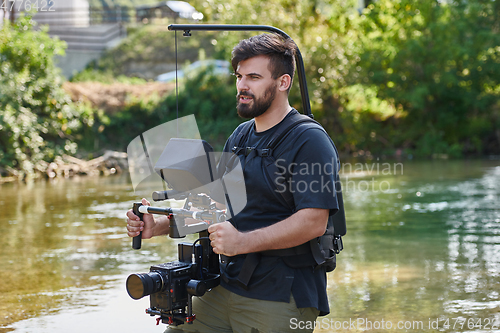 Image of a professionally equipped cameraman shoots in the water surrounded by beautiful nature.