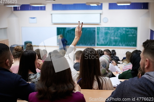 Image of female student sitting in the class and raising hand up