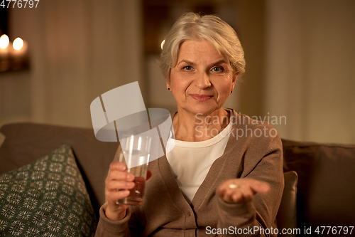 Image of senior woman with water and medicine at home