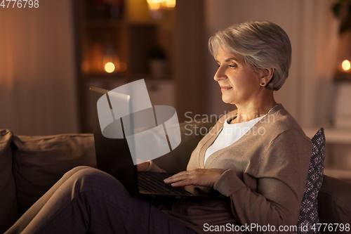 Image of happy senior woman with laptop at home at night