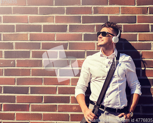 Image of young man in headphones with bag over brickwall
