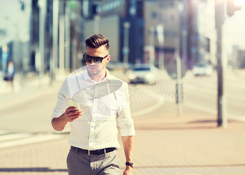 Image of man in sunglasses with smartphone walking at city