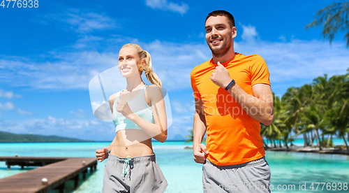 Image of smiling couple running along exotic on beach