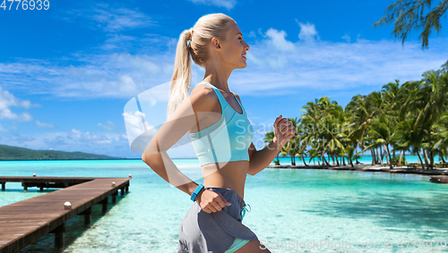 Image of smiling young woman running along exotic beach