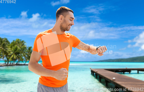 Image of smiling man with smart watch running along beach