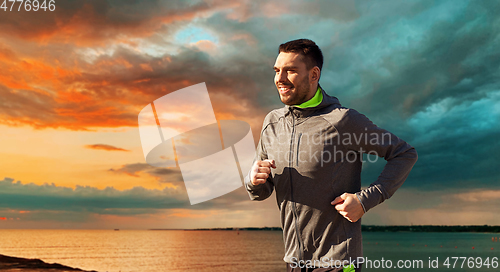 Image of happy young man running over sea and sunset sky