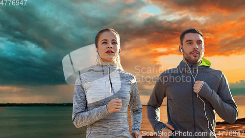 Image of happy couple with earphones running over sea