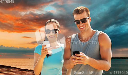 Image of couple in sports clothes with smartphones on beach