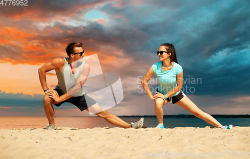 Image of smiling couple stretching legs on beach