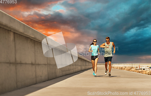 Image of couple in sports clothes running along pier