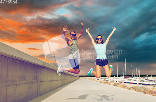 Image of happy couple in sports clothes jumping on pier