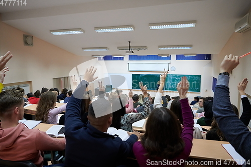 Image of Raised hands and arms of large group of people in class room