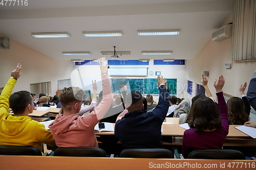 Image of Raised hands and arms of large group of people in class room