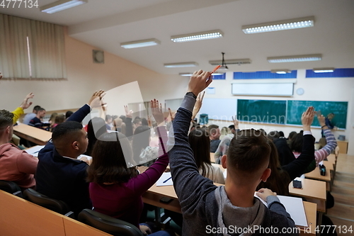 Image of Raised hands and arms of large group of people in class room