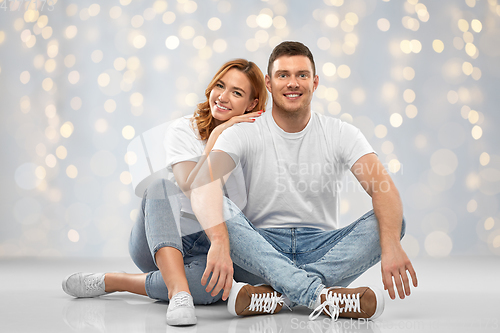 Image of happy couple in white t-shirts sitting on floor