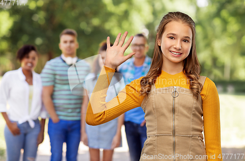 Image of happy teenage girl waving hand over friends