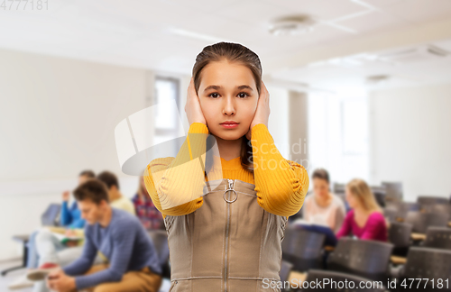 Image of student girl closing ears by hands at school