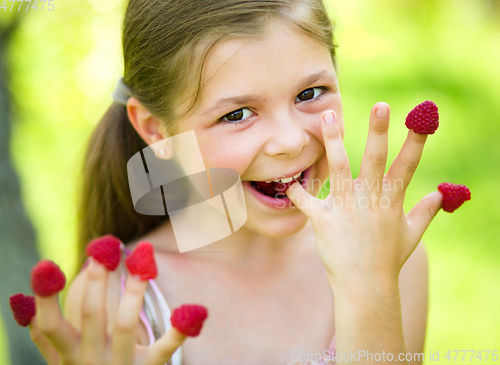 Image of Young girl is holding raspberries on her fingers