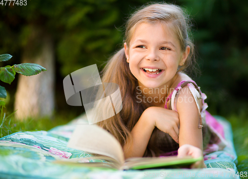 Image of Little girl is reading a book outdoors