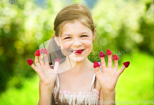Image of Young girl is holding raspberries on her fingers
