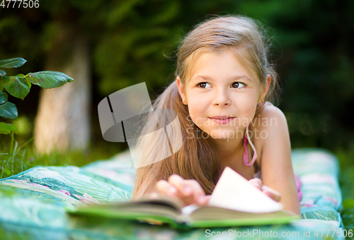 Image of Little girl is reading a book outdoors