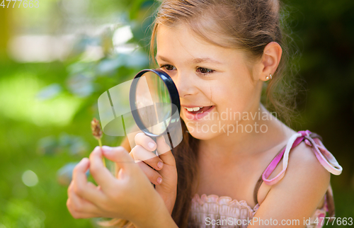 Image of Young girl is looking at flower through magnifier