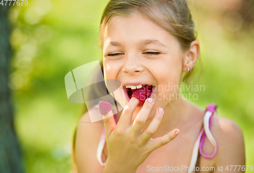 Image of Young girl is holding raspberries on her fingers