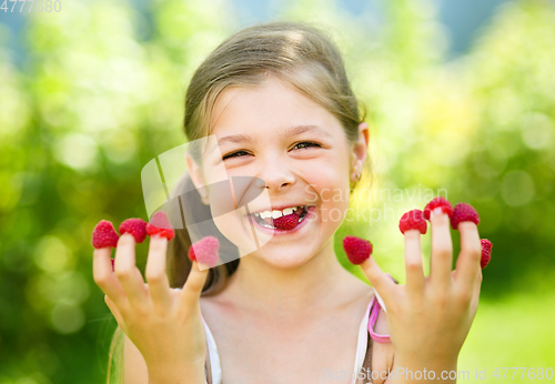 Image of Young girl is holding raspberries on her fingers