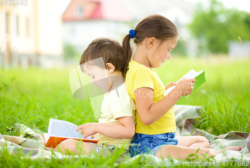 Image of Little girl and boy are reading book outdoors