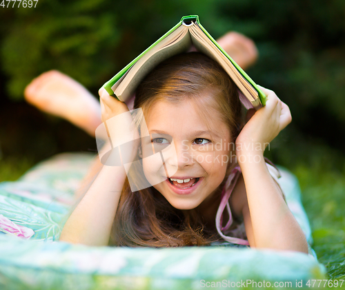 Image of Little girl is hiding under book outdoors