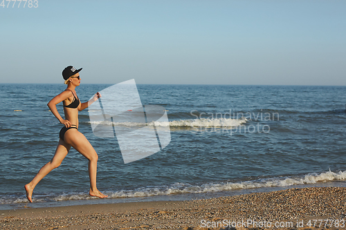 Image of Active sporty woman run along ocean surf by water pool to keep fit and health. Sunset black sand beach background with sun. Woman fitness, jogging workout and sport activity on summer family holiday.