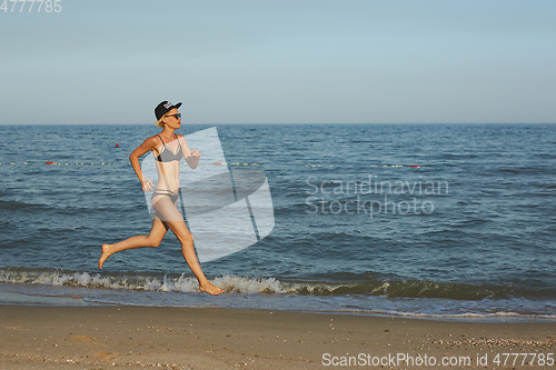 Image of Sexy and happy beautiful woman in bikini running on the beach. In a cap with the inscription queen. Film effect.