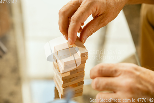 Image of Close up of senior man\'s hands doing his wooden constructor at home - concept of home studying