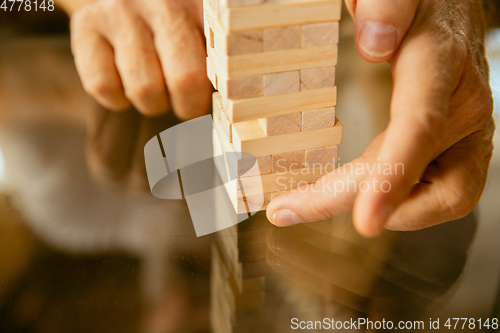 Image of Close up of senior man\'s hands doing his wooden constructor at home - concept of home studying