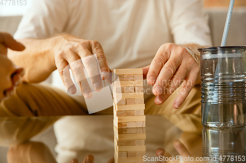 Image of Close up of senior man\'s hands doing his wooden constructor at home - concept of home studying