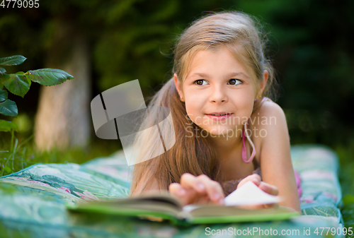 Image of Little girl is reading a book outdoors