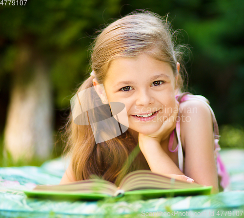 Image of Little girl is reading a book outdoors