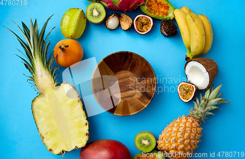 Image of wooden bowl and different exotic fruits on blue