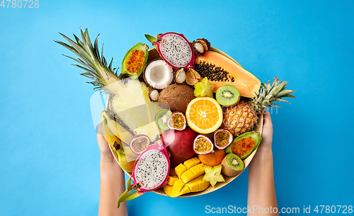 Image of hands holding plate of exotic fruits over blue