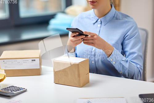 Image of woman with smartphone and parcels at post office